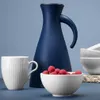 A navy blue carafe is displayed behind a white mug and a white bowl filled with red candies. Voir les images du produit
