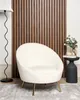 A cream-colored armchair with golden legs sits in a room with a slatted wooden wall. Náhled obrázku produktu