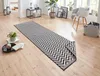 A long runner rug with a black and white chevron pattern is laid out on a light wood floor in a room with natural light coming from a window. Voir les images du produit