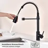 A hand is holding a black kitchen faucet spray head, with water spraying into a glass bowl. The faucet is mounted on a kitchen counter. Podgląd zdjęcia produktu
