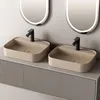 A modern bathroom vanity with two beige ceramic sinks and black faucets, set against a neutral wall with illuminated mirrors above. Produktbild-Vorschau