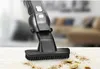 A close-up of a black handheld vacuum cleaner with a brush head on a white surface, with crumbs and debris on the surface. Produktbild-Vorschau