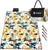 A folded picnic blanket with a tropical pattern and a carrying bag, along with ground stakes. Náhled obrázku produktu