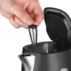 A hand is holding a filter over the opening of a black electric kettle. Náhľad obrázku produktu