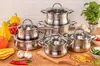A collection of stainless steel pots and pans are arranged on a wooden surface, surrounded by fresh vegetables and pasta. Náhled obrázku produktu