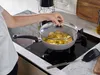A person is cooking with a pan on a stovetop. Produktbild-Vorschau
