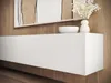 A close-up view of a white, modern, wall-mounted TV lowboard with wooden accents, set against a wooden wall. Decorative items, including a white bowl and a vase with white flowers, are placed on top. Náhľad obrázku produktu
