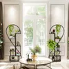 A living room scene with two heart-shaped plant stands filled with plants and books, placed near a large window. A coffee table with a vase of flowers is in the foreground. Produktbild-Vorschau