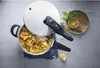 A pressure cooker with food inside, placed on a countertop with some ingredients and herbs nearby. Produktbild-Vorschau
