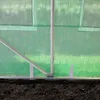 Close-up view of the base of a green transparent greenhouse with a metal frame, showing the ground and the mesh material. Produktbild-Vorschau