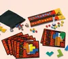 A collection of game pieces, including colorful gems, dice, cards, and puzzle pieces, are arranged on a light beige surface. Produktbild-Vorschau