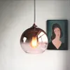 A pendant light with a glass globe and exposed bulb hangs in front of a wall with a painting. Voir les images du produit