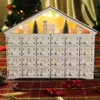 A white wooden advent calendar shaped like a house, decorated with miniature Christmas trees and houses, and illuminated by warm LED lights. The calendar has 24 numbered drawers. Voir les images du produit