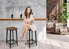 A woman sits on a bar stool next to another bar stool, with a bar counter and drinks in the background, in a room with brick and concrete walls. Podgląd zdjęcia produktu