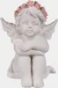 A white cherub figurine with a pink and green rose wreath on its head, sitting with its arms crossed. Produktbild-Vorschau