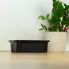 A black plastic storage box is placed on a wooden floor next to a potted plant and a white wall with an electrical outlet. Anteprima dell’immagine prodotto