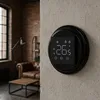 A modern digital thermostat is mounted on a textured wall in a living room with exposed brick and leather furniture. Náhled obrázku produktu
