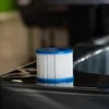 A close-up shot of a white pool filter cartridge with blue rims, resting on a dark, reflective surface. Produktbild-Vorschau