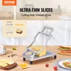 A cheese slicer with a block of cheese on it, along with sliced cheese and other food items on a table. Voir les images du produit