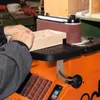 A person is using a belt sander to smooth a wooden box in a workshop. Podgląd zdjęcia produktu