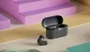 A pair of gray wireless earbuds and their charging case are displayed on a multi-colored surface with abstract geometric shapes in the background. Produktbild-Vorschau