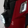 Close-up of the front of a red three-wheeled vehicle, showing the headlight and a turn signal. Produktbild-Vorschau
