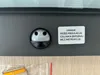 Close-up of a motion sensor on a dark gray product, with a warning sticker next to it. Anteprima dell’immagine prodotto
