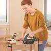 A woman is using a jigsaw to cut a piece of wood in a workshop or home setting. Náhled obrázku produktu