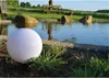 A white spherical garden light is placed in the foreground next to a pond, with a dog and a wooden bench in the background. Produktbild-Vorschau