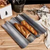 Two baguettes are placed on a perforated baking sheet on a wooden table, with a decorative paper bag and a metal bucket in the background. Náhled obrázku produktu