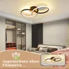 A modern bedroom with a ceiling light, closet, and bed, with a hand holding a phone showing the same light. Voir les images du produit