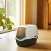 A cat litter box with a hood and swing door is placed on a wooden floor next to a window with a plant. Produktbild-Vorschau