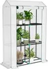 A white greenhouse with a roll-up door, containing multiple shelves filled with potted plants. Produktbild-Vorschau