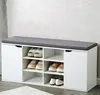 A white shoe cabinet with a gray cushion on top, filled with shoes, placed against a textured wall. Náhľad obrázku produktu