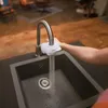 A person's arm is shown reaching towards a kitchen sink faucet with a BRITA ON TAP water filter attached, and water is running into the sink. Produktbild-Vorschau