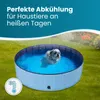 A small dog is enjoying a dip in a blue, round dog pool set up on a grassy lawn. Produktbild-Vorschau