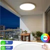 A modern balcony at dusk with a round LED ceiling light illuminating the space. A small wooden table and chairs are set up, with potted plants on the balcony. Produktbild-Vorschau