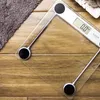 A close-up view of a digital bathroom scale on a wooden floor, with a grey towel to the left. Náhled obrázku produktu