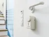 A close-up shot of a white door handle and a white electronic device mounted on a white wall. Náhľad obrázku produktu