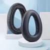 Two black headphone ear pads are displayed on white pedestals against a light blue and white background. Produktbild-Vorschau