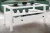 A white coffee table with a glass top, a shelf, and a drawer, placed in a living room setting with a green sofa in the background. Produktbild-Vorschau