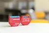 Two red smart home devices are placed on a white surface with a blurred background. Produktbild-Vorschau