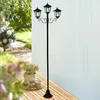 A black metal solar candelabra with three lights stands on a wooden deck next to a basket of flowers. Produktbild-Vorschau