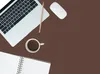 A flat lay of a laptop, mouse, coffee mug, pencil, and notebook on a brown surface. Produktbild-Vorschau