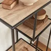 A close-up view of a multi-tiered shelf unit with a wood-grain finish and black metal frame. Decorative boxes and a bowl are placed on the shelves. Produktbild-Vorschau