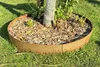 A tree ring made of Corten steel is placed around the base of a tree in a grassy yard, filled with mulch. Produktbild-Vorschau
