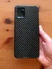 A hand holding a smartphone with a carbon fiber skin on the back. Produktbild-Vorschau