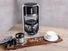 A coffee maker with a carafe, a cup of tea, and loose tea leaves are arranged on a wooden countertop. Náhled obrázku produktu