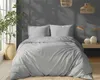 A neatly made bed with light gray striped satin bedding, set against a dark gray wall with natural light streaming in from a window. A potted plant and decorative items add to the room's ambiance. Anteprima dell’immagine prodotto