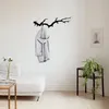 A coat rack shaped like a tree branch hangs on a white wall, with a coat draped over it. A sofa and a side table with a plant are also visible. Náhled obrázku produktu
